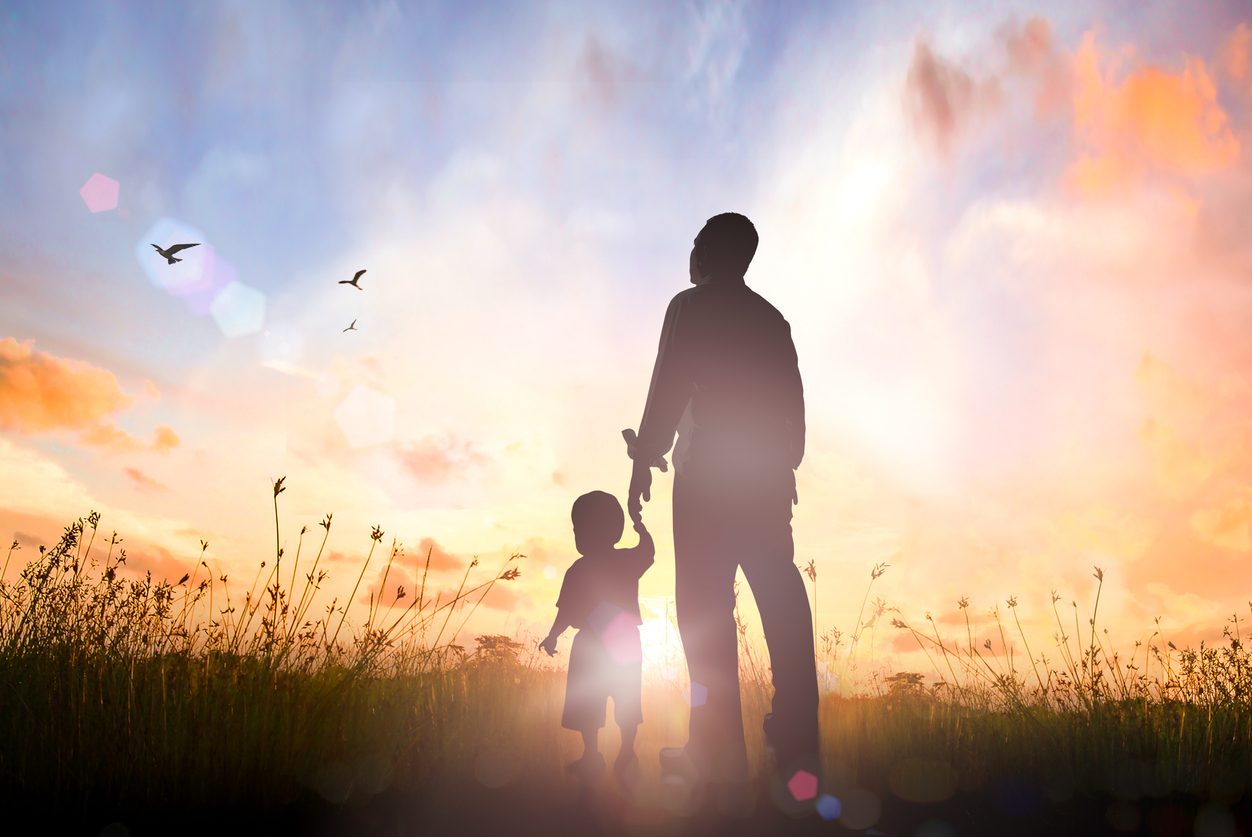 A parent and child silhouetted against a sunrise